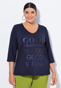 Navy V-Ausschnitt Langarmshirt mit metallischen Buchstaben in verschiedenen Farbtönen, mit auffällig auf der Vorderseite gedruckten Phrasen.