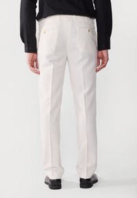 Weiße, maßgeschneiderte Hose aus leichtem Stoff. Sie verfügt über zwei Gesäßtaschen mit goldfarbenen Knöpfen, gerade Beine und eine glatte Textur.