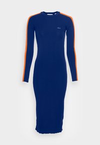 Mörkblå stickad klänning med långa ärmar, med orangea ränder längs axlarna. Tätsittande silhuett med en scalloped nederkant.