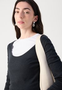 Juodas ilgomis rankovėmis viršutinis drabužis, uždėtas ant balto marškinėlio su apvalia kaklo iškirpte. Turi išpjautą kaklo liniją ir lygią, minkštą tekstūrą. Balto rankinio diržas.