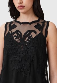 Čierny tielkový top s priesvitnou látkou, zdobený zložitým kvetinovým vyšívaním a vrúbkovaným výstrihom. Mäkká textúra s jemnými detailmi.