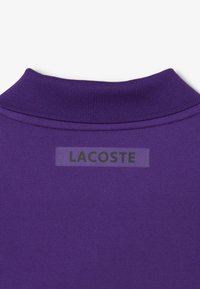 Paarse polo-shirt kraag met een textuurstof, met een prominente 'LACOSTE' logo-tag genaaid op de achterkant.