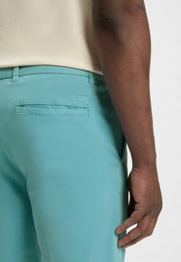 Turkusowe bawełniane spodnie z tylną kieszenią i metką "BOSS". Slim fit, gładka tekstura i dopasowana talia.