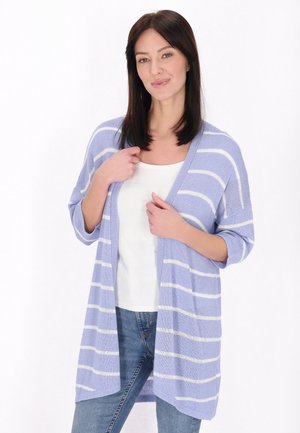 Cardigan violet deschis cu dungi orizontale albe, deschis în față, cu mâneci scurte, dintr-un material texturat și cu un croi relaxed. Poartă un top alb și blugi albaștri.