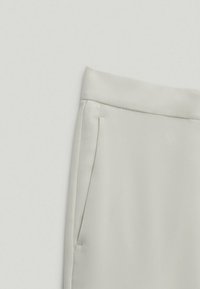 Pantalons taillés beige clair avec une texture lisse, dotés d'une taille plate et de poches latérales. Le tissu a un éclat subtil.