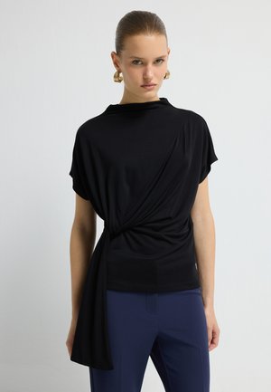 Haut noir avec un design drapé, présentant une section torsadée à la taille. Tissu doux, manches courtes, associé à un pantalon bleu marine.