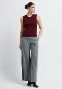 Top sin mangas burdeos, diseño ajustado, combinado con pantalones de cuadros grises de pierna ancha, metido por dentro. Accesorios con pendientes de plata y tacones negros.