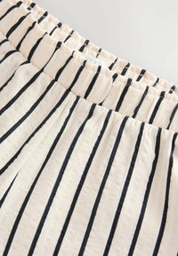 Tissu léger à nervures avec une base crème et des rayures verticales bleu marine. Doté d'une taille élastique pour un confort optimal et une facilité de port.
