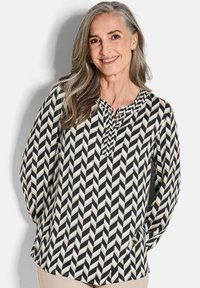 Chemisier à manches longues avec un motif en chevrons noir, blanc et beige ; présente un col en V et un tissu fluide.