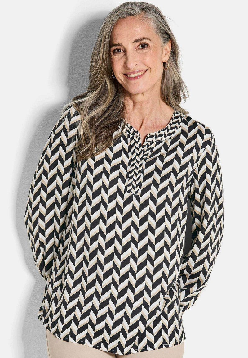 Chemisier à manches longues avec un motif en chevrons noir, blanc et beige ; présente un col en V et un tissu fluide.