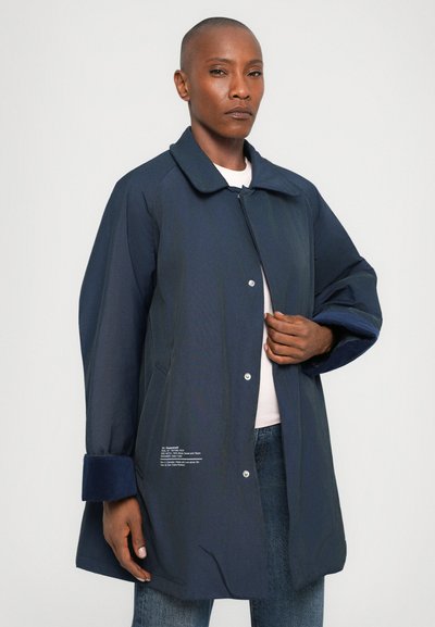 Navy jacket with a collared neck, snap button closure, and side pockets. Features soft blue cuffs and text details on the lower side.