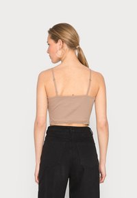 Top curto castanho com alças finas, com rendinha na bainha, combinado com calças pretas de cintura alta. Design simples e ajustado ao corpo.