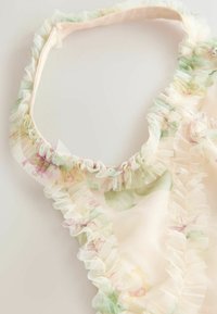 Tissu floral transparent avec bords froncés et fine bretelle élastique, probablement une pièce de lingerie ou un vêtement délicat.