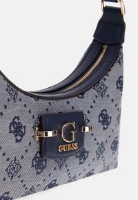 Navy blue handbag with denim texture, featuring a gold hardware logo and zip closure. Distinctive pattern in darker blue accents.