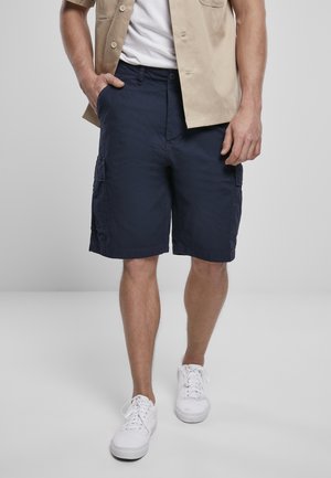 Marineblauwe cargoshorts gemaakt van lichtgewicht stof, met zijzakken en een losse pasvorm, gecombineerd met witte sneakers en een beige overhemd.