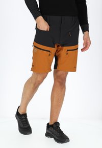 Heren shorts in zwart en oranje, gemaakt van lichtgewicht materiaal. Bevat twee met rits afgesloten zakken en heeft een klassieke pasvorm. Draagt met zwarte wandelschoenen.