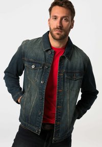 Chaqueta de denim en azul oscuro con un acabado desgastado, cuenta con botones a presión, dos bolsillos en el pecho y un cuello clásico, combinada con una camisa roja.