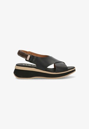 Sandalia de piel negra tipo slingback con diseño de correas cruzadas, suela acolchada y un acento metálico texturizado en la correa trasera ajustable.