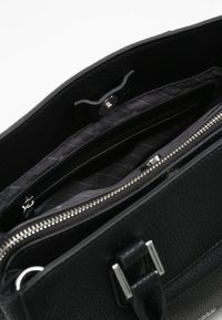 Sac à main en cuir noir avec un extérieur texturé, des compartiments zippés et un intérieur en satin lisse. Contient plusieurs poches pour l'organisation.