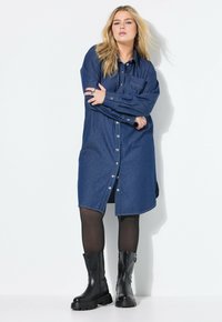 Denim-mekko tummansinisessä värissä, jossa on pitkät hihat, etutasku ja napitus, yhdistettynä mustiin sotilasbootsiin.