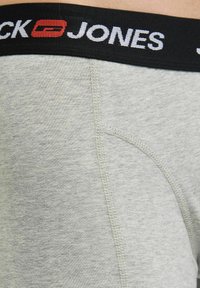 Pilki medvilniniai bokseriai su juodu elastingu juosmuo, ant kurio matomas baltas ženklas; sklandžiai tekstūruoti, su tiksliomis siuvimo detalėmis.