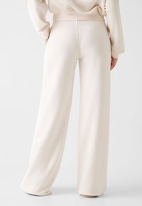 Szerokie spodnie o kremowym kolorze wykonane z miękkiej tkaniny; cechują się gładką fakturą i brakiem widocznych wzorów lub dodatków.