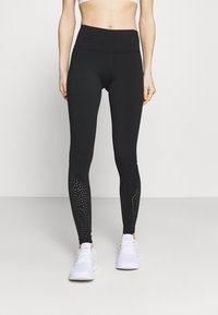 Leggings noirs en tissu extensible avec une taille haute. Présentent des accents texturés avec des motifs cloutés près de la cheville.
