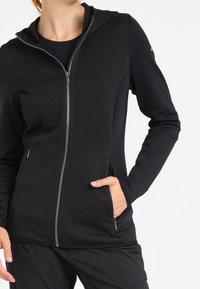 Giacca nera con cappuccio caratterizzata da un pannello frontale testurizzato, chiusura con zip completa e tasche laterali; realizzata in un materiale liscio e elastico.