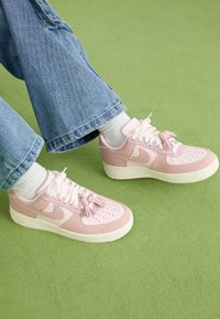 Zapatillas de cuero rosas con suelas y cordones blancos, con puntera perforada y acentos de borlas. Combinadas con pantalones de mezclilla anchos y calcetines blancos.