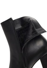 Bottines en cuir noir avec doublure en fourrure, dotées d'une fermeture éclair sur le côté et d'une partie supérieure repliée. Design à talon carré. Fini mat.