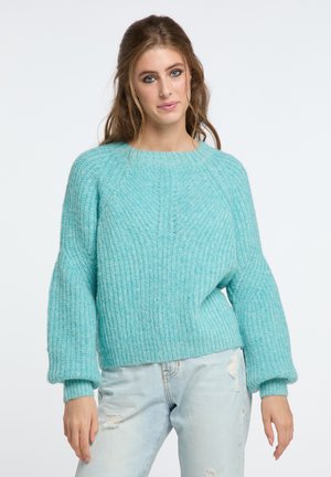 Turquoise knitted sweater with a textured pattern, round neckline, and slightly puffed sleeves. Paired with light distressed denim jeans.