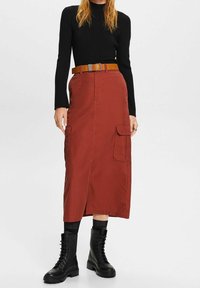 Bordauxfarbene Cargorock mit einem vorderen Schlitz, zwei seitlichen Taschen und einem braunen Gürtel. Kombiniert mit schwarzen Schnürstiefeln. Gestreiftes schwarzes Langarmoberteil.