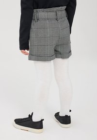 Pantaloni corti grigi a scacchi con vita regolabile e risvolti. Le calze bianche e le sneakers nere completano l'outfit.