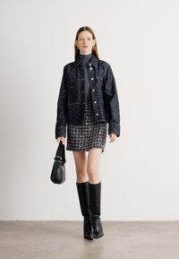 Crni uzorčani sako preko sive turtleneck majice, uparen s teksturiranom suknjom i crnim čizmama do koljena. Uključena je i mala crna torbica.