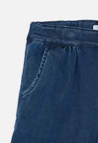 Traperice tamnoplave boje, s rastezljivim pojasom, bočnim džepom i glatkom teksturom. Ležeran dizajn s detaljima šivanja.