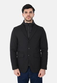 Giacca nera su misura con rever a lancia, tre bottoni, due tasche frontali e un rivestimento interno trapuntato. Design casual con una finitura elegante.