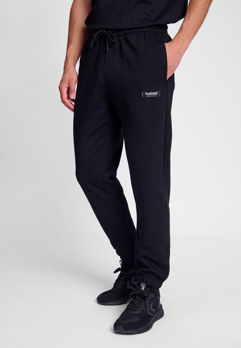 Schwarze Jogginghose mit elastischem Bund und verstellbarem Kordelzug. Sie verfügt über Seitentaschen und ein kleines Logo am linken Oberschenkel.