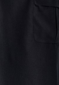 Kamniti posnetek črnega blaga, ki prikazuje pravokotno šivano žep na desni strani.