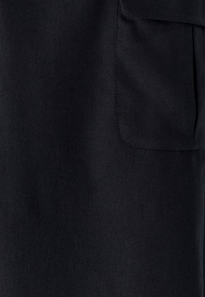 Nahaufnahme von schwarzem Stoff mit einer rechteckigen genähten Tasche auf der rechten Seite.