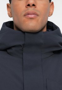 Granatowa kurtka z wysokim kołnierzem, wykonana z miękkiego, gładkiego materiału, z zamkiem błyskawicznym i przednią kieszenią. Czysty, minimalistyczny design.
