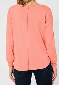 Långärmad korallfärgad sweatshirt med rund halsringning, en mittsöm längs ryggen, samt ribbade nätkanter och manschetter. Mjuk, elastisk tyg.