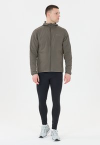 Lätt, olivgrön zip-up jacka med huva, sidofickor och slät textur, parat med svarta träningsleggings och löparskor.