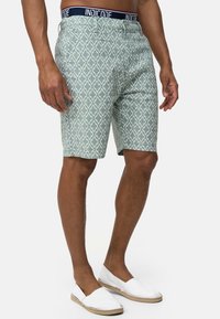 Shorts vert clair à motif géométrique, avec une taille marine portant l'étiquette "INDICODE". Le matériau semble lisse et léger.