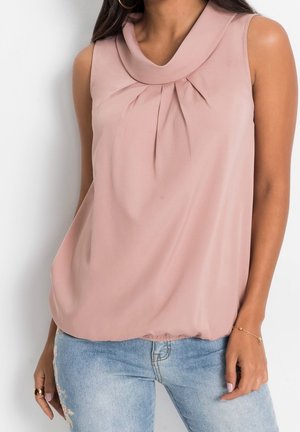 Hihaton posliininpunainen pusero laskostetulla laahuskaula-aukolla, yhdistetty vaaleansinisiin kirjailtuihin farkkuihin ja kultaisiin renkaanmuotoisiin korvakoruihin.