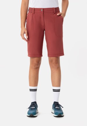 Shorts rouges arrivant au-dessus des cuisses avec un devant plat, deux poches latérales et une ceinture texturée. Associés à des baskets bleues et des chaussettes blanches rayées.