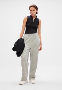 Czarny top bez rękawów z zamkiem i szare dresy. Model trzyma czarną bluzę. Codzienny strój o miękkich fakturach i luźnym kroju.