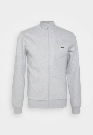 Veste gris clair zippée intégrale avec col montant, manches longues, poignets et bas côtelés, avec petit logo crocodile vert sur la poitrine.