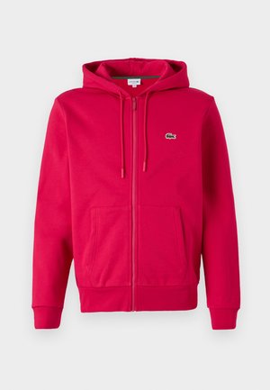 Sweat à fermeture éclair rouge en mélange de coton, avec une poche kangourou, un capuchon à cordon de serrage et un petit logo vert sur la poitrine.