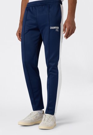 Pantalones deportivos azul marino con rayas blancas en los costados, cintura elástica y logo de "Champion F.C." en el muslo izquierdo. Textura de tela suave.