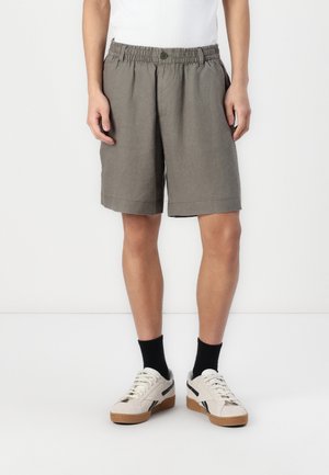 Shorts en tissu gris avec une taille élastique et un bouton, présentant une coupe décontractée et un design à longueur genou, assortis à des baskets blanches.